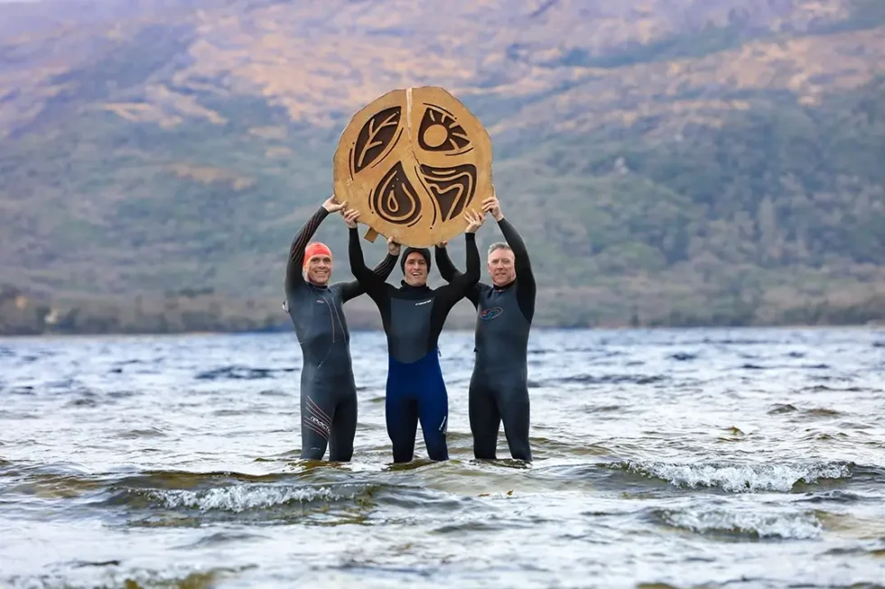 Wander Wild festival group of three men holding festival logo in lake water
