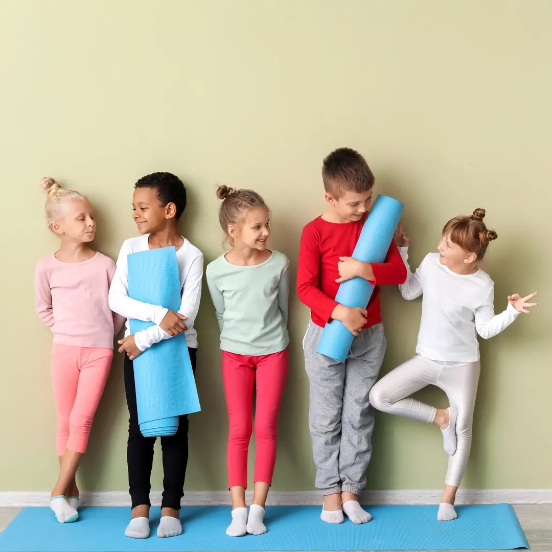 Little children with yoga mats near colour wall in gym