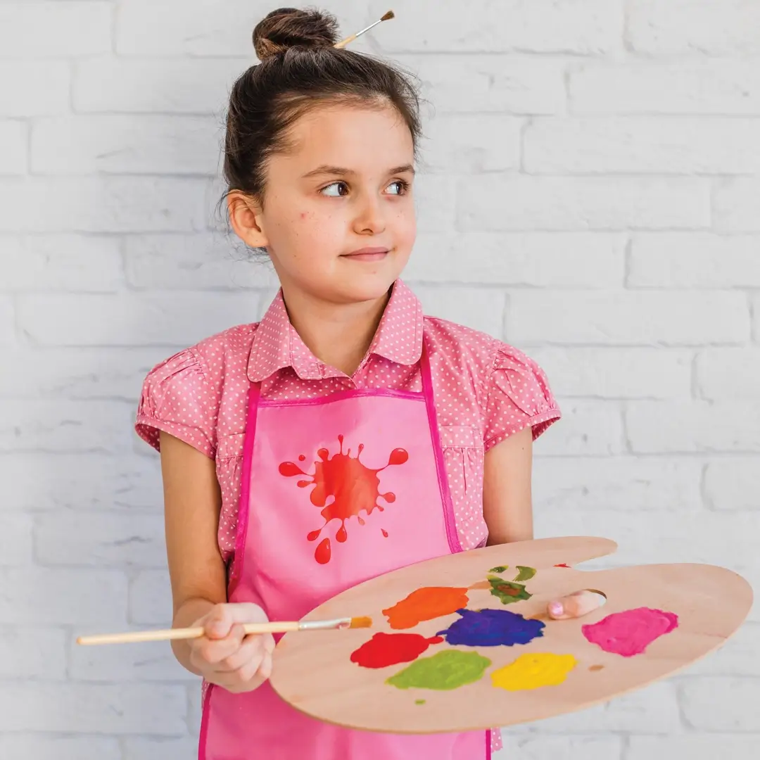 Girl standing against white brick wall holding palette and paintbrush