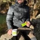 A man eating a bar drinking from a mug